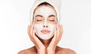 Beautiful woman with eyes closed and white clay facial mask on face isolated on white background